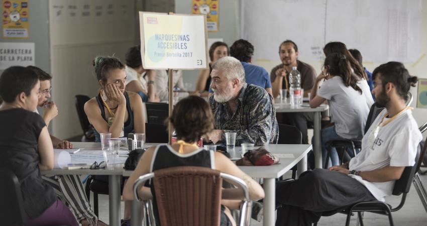 Personas hablando alrededor de una mesa, rótulo "marquesinas accesibles"