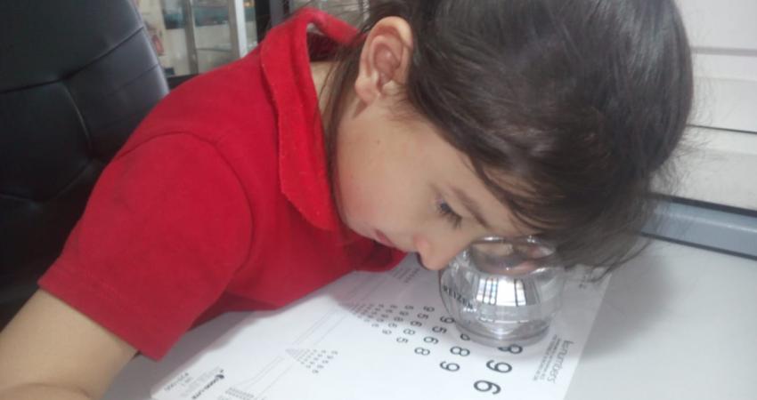 niña con baja visión mirando leyendo un documento con una lupa